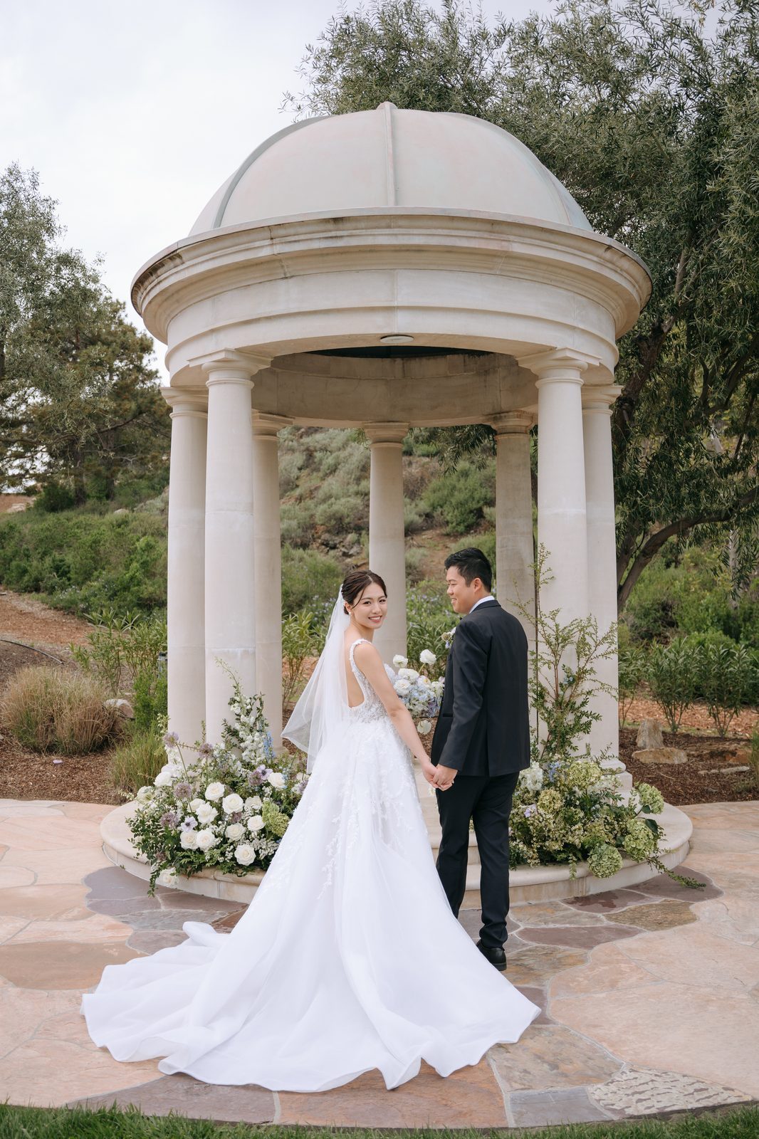 Couple holding hands at a garden gazebo surrounded by florals